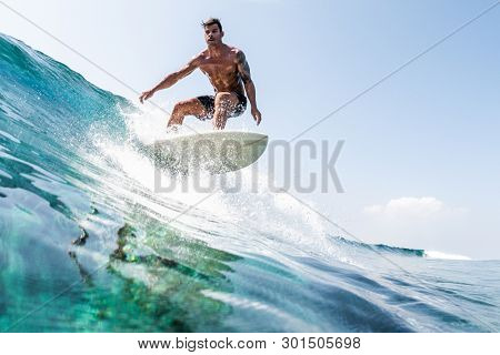 HIMMAFUSHI / MALDIVES - MARCH 11, 2019: Young hispanic man surfs the glassy ocean wave at sunny day