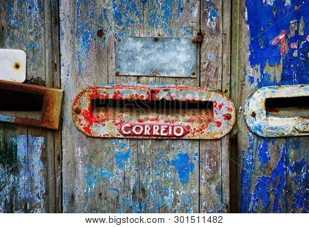 Three old mailboxes in an damaged wooden door with peeling blue paint. Correio means Mail.