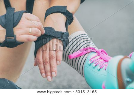 Woman rollerskater putting on wrist guards protector pads on her hand