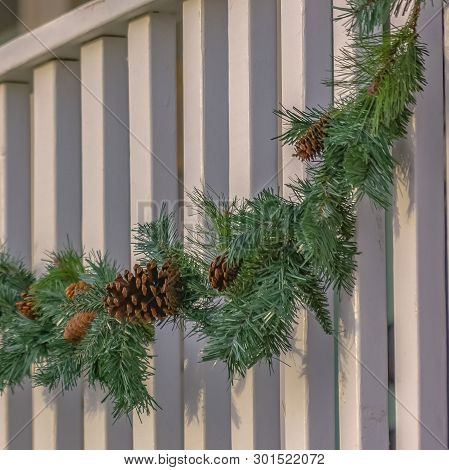 Square Traditional Garland With Pine Cones Draped On The White Railing Of A Building