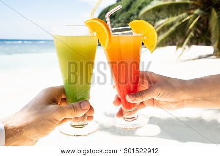 Couple's Hand Toasting The Glasses Of Cocktail At Beach