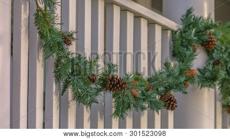 Traditional Garland With Pine Cones Draped On The White Railing Of A Building