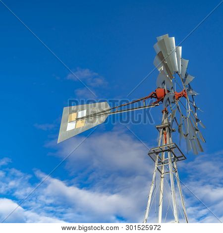 Square Close Up Of A Windpump With Vibrant Blue Sky And Puffy Clouds In The Background