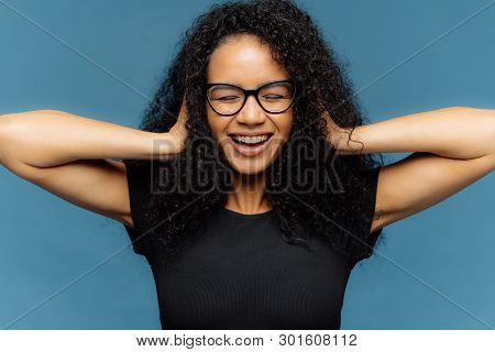 Photo Of Lovely Smiling Afro Female With Crsip Hair, Covers Ears, Being In Good Mood, Wears Casual B