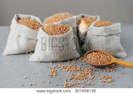 Husbandry Concept. Raw Buckwheat In Sacks, Wooden Spoon Near, Splited Cereals, Isolated Over Grey Ba