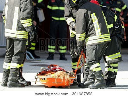 Stretcher With The Wounded And The Group Of Firefighters Who Saved The Injured Person After The Seri