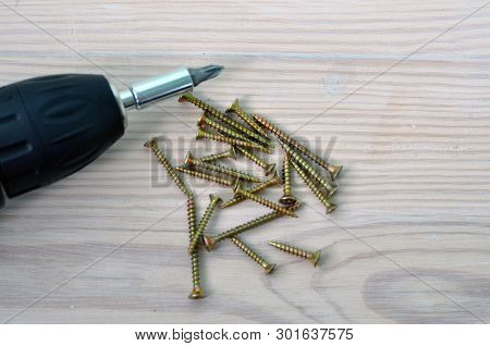 Electric Screwdriver And Screws On A Wooden Table.