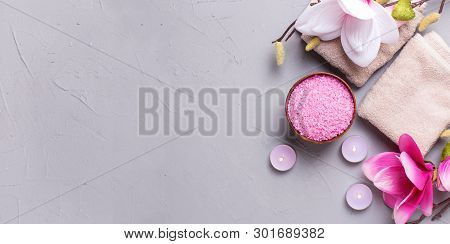 Towels, Sea Salt In Bowl, Burning Candles And Pink Magnolia Flowers On Grey Textured Background. Spa