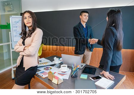 Asian Businesswoman Standing With Disregard The Workmate Who Are Standing And Shaking Hand In Backsi