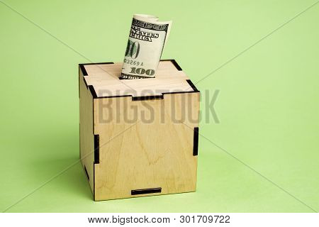 Depositing Hundred Dollar Bill Into Moneybox On The Green Background.