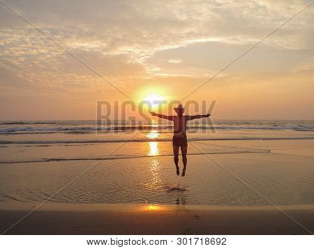 At Sunset, A Happy Man In A Hat Jumps Out Of The Water For Joy