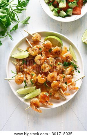 Grilled Prawns Skewers With Greens, Spices, Lime And Sauce On White Plate Over Wooden Table. Tasty S