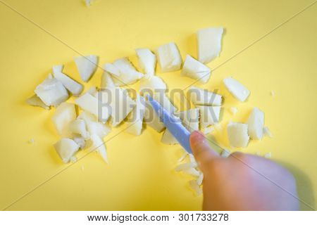 Kid Cuts With A Toy Knife Potatoes In Kitchen. Boiled Potato Pieces And Hand Of Toddler On A Backgro