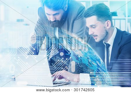 Two Young Men In Suits Working In Office With Laptop. Double Exposure Of Planet And Circuit Interfac