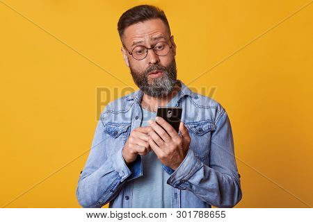 Close Up Portrait Of Middle Aged Caucasian Man Using Smarphone With Shocked And Surprised Face Expre