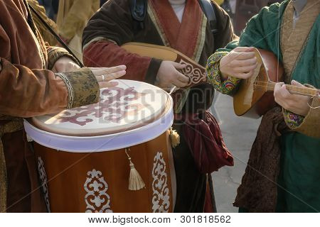 Street Musicians In National Costumes Play Folk Instruments - A Drum And A Dombra During A Holiday