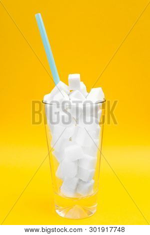 Close Up Of Glass Full Of Sugar Cubes Over Yellowbackground. Unhealthy Diet And Diabetes Concept. Co
