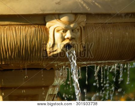 A Fragment Of An Old Fountain With A Human Head And A Stream Of Water Flowing From The Mouth.a Commo