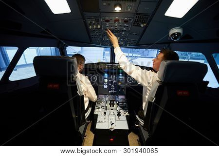 Rear View Of Serious Busy Young Aviators In White Shirts Sitting At Airplane Dashboard And Making Pr