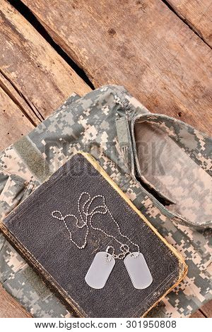 In Memory Of A Brave Soldier. Military Camouflage Clothes, Old Book, And Dog Tags On Wood.