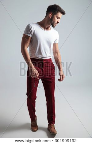Confident looking guy stepping and looking to the side while holding his glasses and wearing a white t-shirt on gray studio background