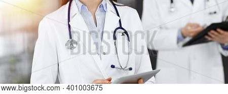 Unknown Woman Doctor Iusing Tablet Computer In Her Hands, While Standing In Sunny Clinic. Medicine C