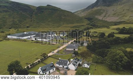 Arran whiskey distillery aerial. Road in green mountains valley. Scottish village with cottages, houses, camp. Rural landscape of coutryside street at summer. Cinematic Scotland alcohol industy shot