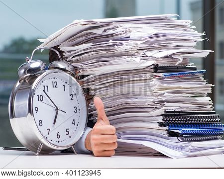 Businessman with pile stack of paper paperwork and an alarm cloc