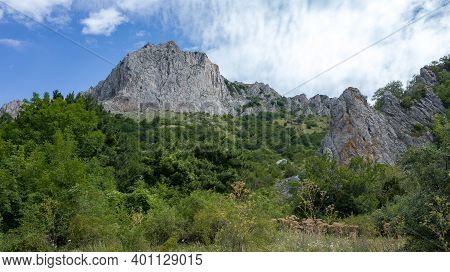 Inaccessible Rocks Surrounded By Green Forests And Shrubs In Hot Summers In Clear Sunny Weather.