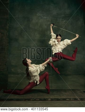 Fight. Two Young Female Ballet Dancers Like Duelists With Swords On Dark Green Background. Caucasian