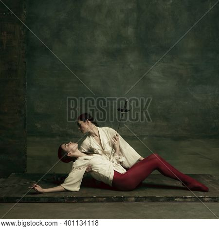 Tragic. Two Young Female Ballet Dancers Like Duelists With Swords On Dark Green Background. Caucasia