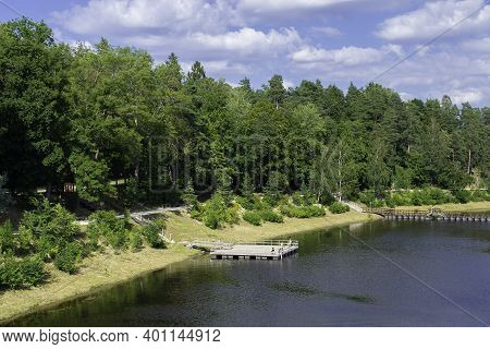 Bank Of The Ogre River In The Town Of Ogre. The Embankment Is Overgrown With Forest And A Pantone Br