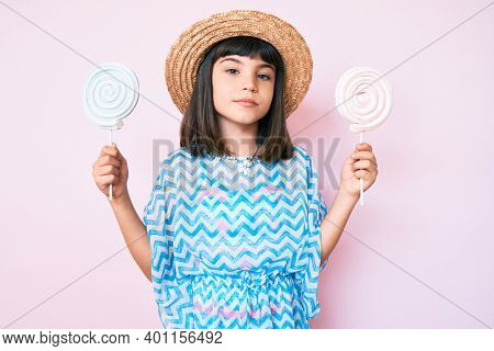 Young little girl with bang wearing summer dress eating candy relaxed with serious expression on face. simple and natural looking at the camera. 