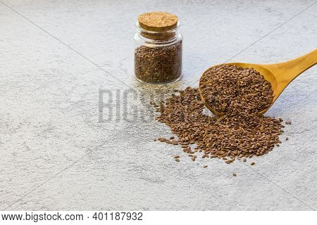 Flax Seeds In A Wooden Spoon And A Glass Jar On Concrete Background, A Dietary Product That Reduces