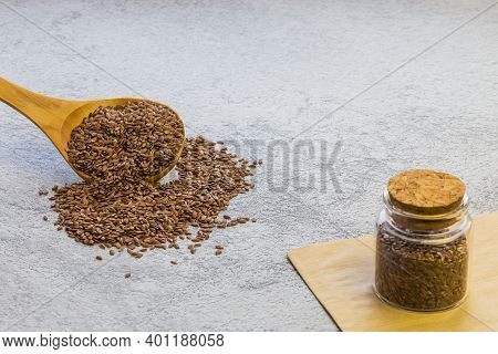 Flax Seeds In A Wooden Spoon And A Glass Jar On Concrete Background, A Dietary Product That Reduces 