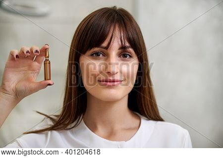 A Beautiful Woman Holds An Ampula Of Dark Glass At The Level Of Her Face