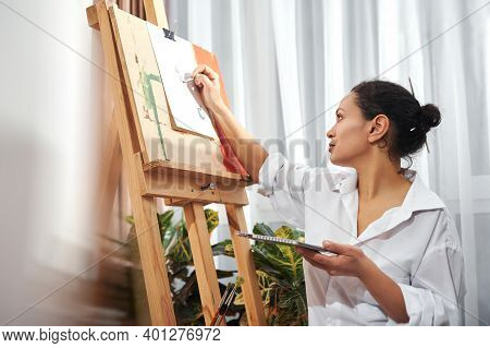 Side View Of Beautiful Brunette Painter With Gathered Hair In A Bun And Paint Brushes In Her Hair Dr