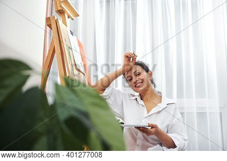 A Beautiful Smiling Artist Holding A Sketch Book In One Hand And Pencil In The Other