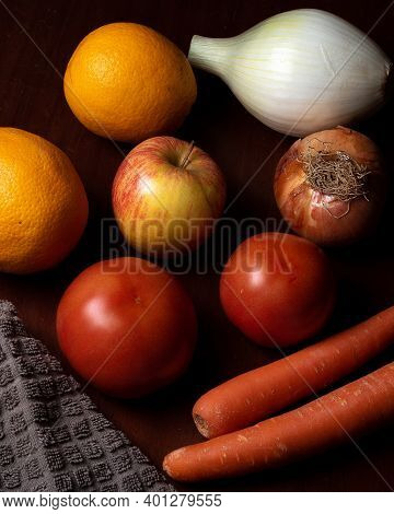 Still Life Of Vegetables And Fruits With Tomato, Onion, Carrot, Orange And Apple In A Dark Brown Tab