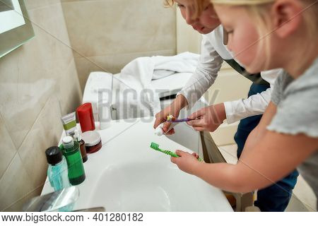 Close Up Of Hands Of Two Children, Boy And Girl Holding Toothbrushes, Squeezing Toothpaste From The 
