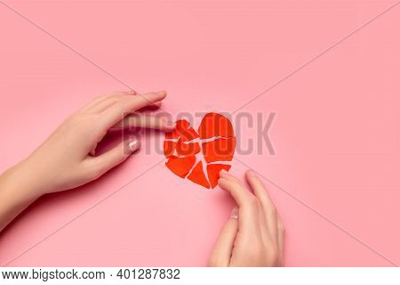 Female Hands Gluing Together Broken Heart, Pieces Of Torn Red Valentine On Pink Background. The Conc