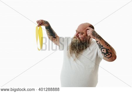 An Overweigh Man Mysteriously Lookings At A Fitness Band While Thinking How To Use It.