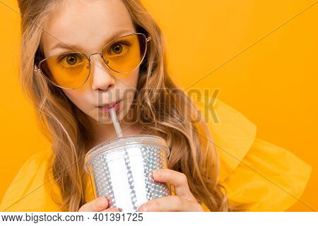 Portrait Of Young Caucaian Girl With Long Fair Hair In Yellow Glasses Drinks A Juice And Smiles