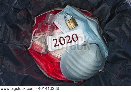 Goodbye 2020 Concept: The Inside Of A Trashbin With Surgical Masks, Sanitizing Gel, A Padlock And A 