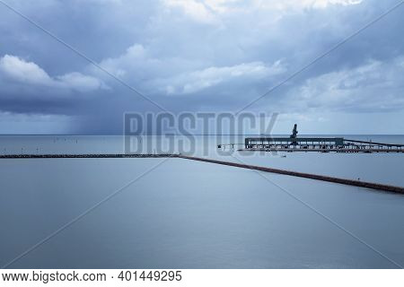 A Boat In The Harbor Enclosed By A Marina Rock Wall, With An Industrial Jetty On The Side, And A Sto