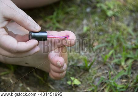 Woman Painting Her Toes With Pink Nail Polish In The Grass