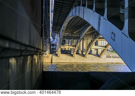 Powerful Iron Bridge Structure, View From Below. Concrete Pillars, Big Iron Rivets. A River Flows Un