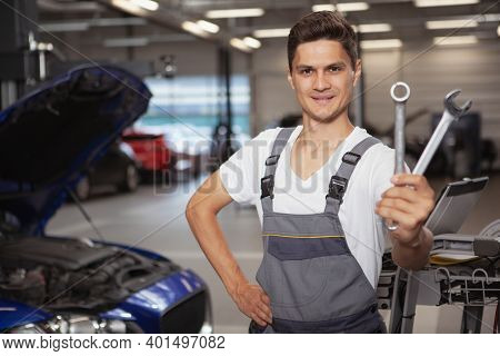 Happy Handsome Young Car Mechanis Smiling, Holding Out His Repair Tools To The Camera. Cheerful Auto