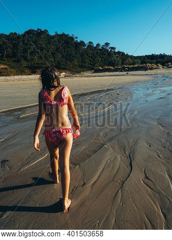 The Image Shows A Back View Of An Unrecognizable Little Girl Walking On The Wet Sand Out Of The Wate