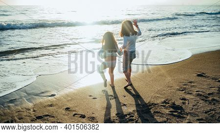 The Picture Shows A Back View Of Two Unrecognizable Little Girls Holding Hands In Front Of The Sea O